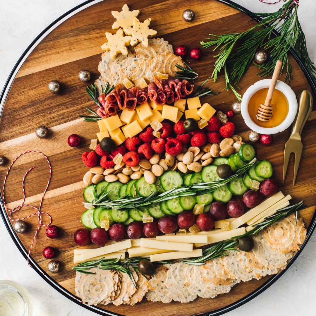 Christmas tree-shaped charcuterie board layered with crackers, cheese cubes, salami, raspberries, almonds, cucumber and grapes