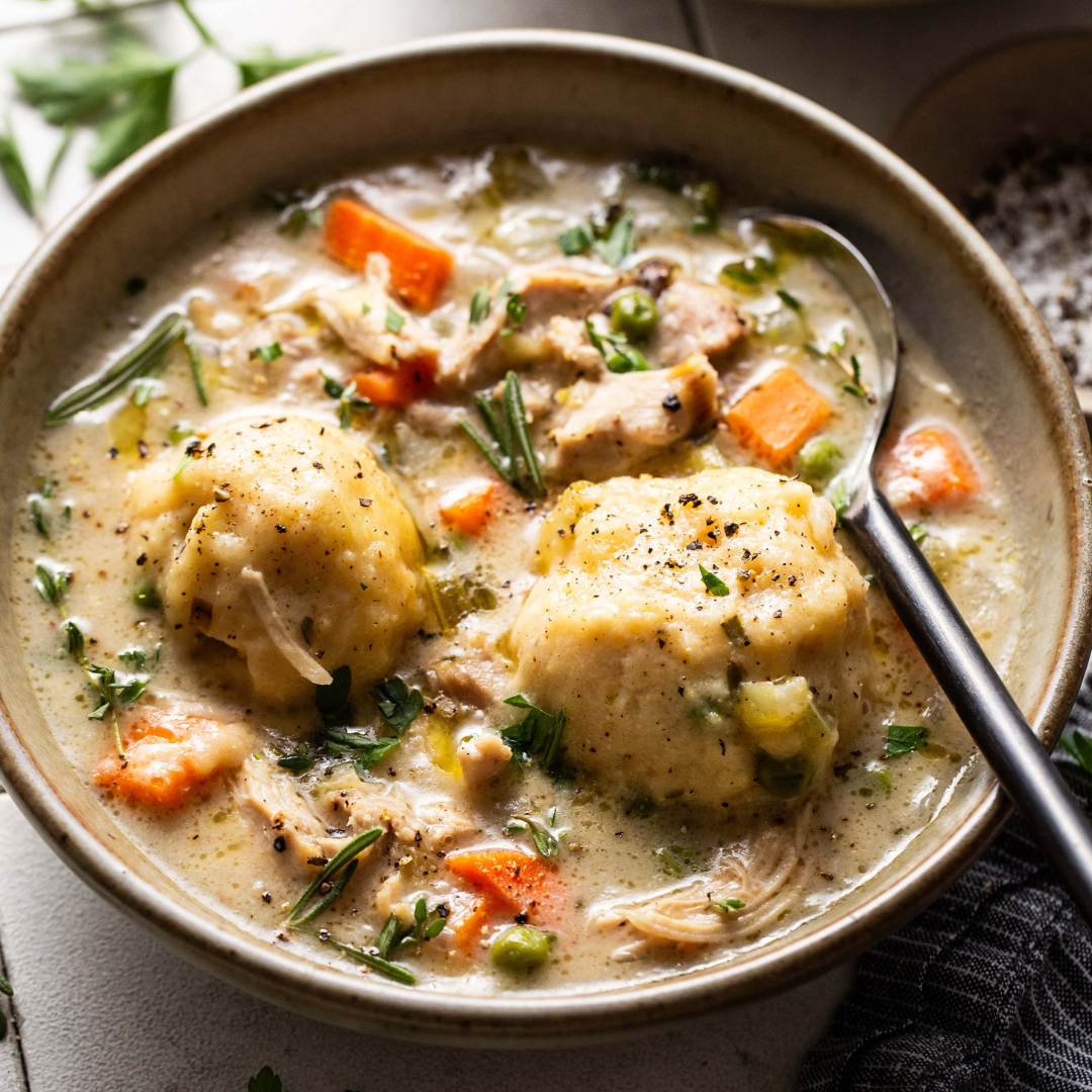 Bowl of homemade chicken and dumplings with carrots, peas, and fresh herbs