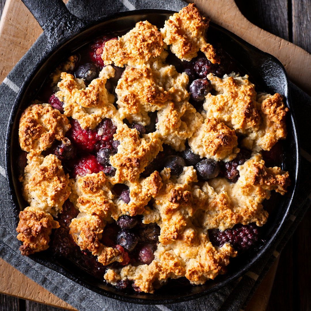 Cast iron skillet mixed berry cobbler with golden drop biscuit topping