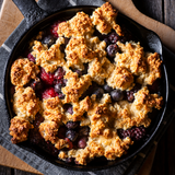 Cast iron skillet mixed berry cobbler with golden drop biscuit topping