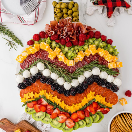 Christmas ornament-shaped charcuterie board with rows of salami, pepperoni, mozzarella balls, star-cut cheese, berries and kiwi