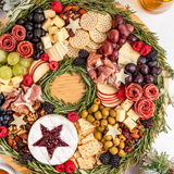 Holiday wreath charcuterie board ringed with rosemary, with brie topped with a jam star, salami roses, prosciutto, olives and berries
